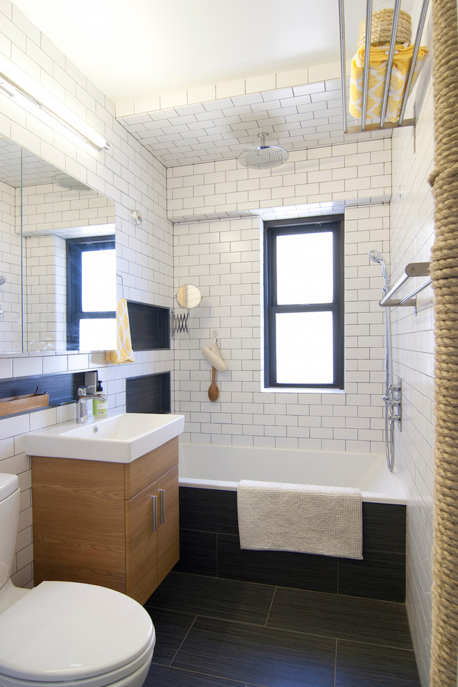 Small modern master bathroom in New York with an alcove tub, a shower/bathtub combo, white tile, white walls, flat-panel cabinets, light wood cabinets, a two-piece toilet, subway tile, porcelain floors, black floor, an open shower and a console sink.