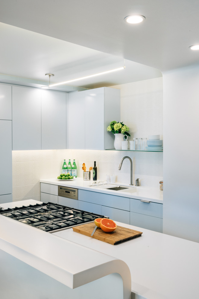 Inspiration for a small contemporary galley kitchen in New York with an undermount sink, flat-panel cabinets, blue cabinets, white splashback, porcelain splashback, stainless steel appliances and with island.