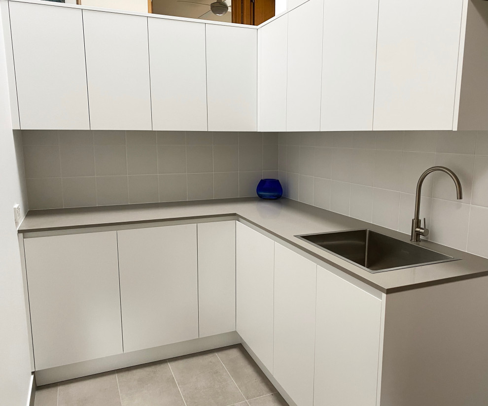 Large modern l-shaped dedicated laundry room in Sydney with a drop-in sink, flat-panel cabinets, white cabinets, quartz benchtops, grey splashback, ceramic splashback, grey walls, porcelain floors, a stacked washer and dryer, grey floor, grey benchtop, vaulted and brick walls.