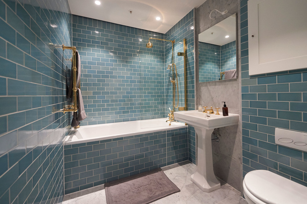 Photo of a mid-sized transitional master bathroom in London with a drop-in tub, a shower/bathtub combo, a wall-mount toilet, blue tile, blue walls, marble floors and a pedestal sink.
