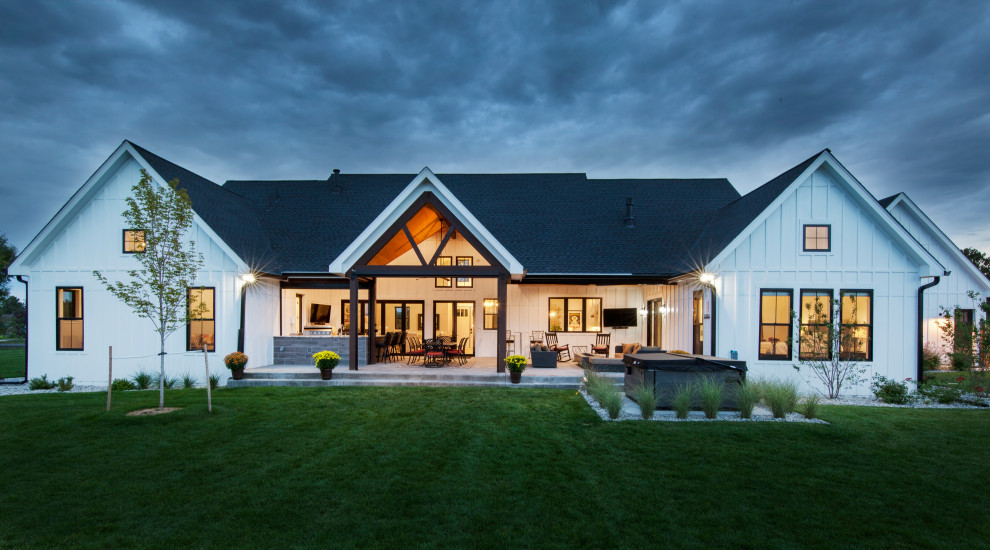 Réalisation d'une grande façade de maison blanche champêtre en panneau de béton fibré et planches et couvre-joints de plain-pied avec un toit à deux pans, un toit mixte et un toit noir.