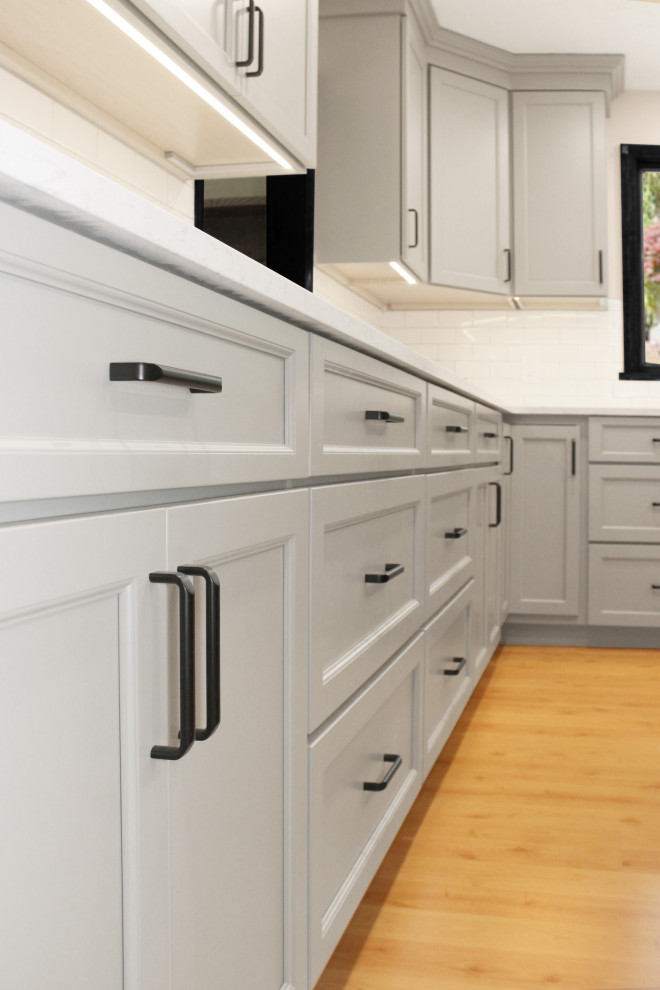 Enclosed kitchen - large transitional u-shaped light wood floor and brown floor enclosed kitchen idea in Boston with a double-bowl sink, shaker cabinets, gray cabinets, quartz countertops, white backsplash, porcelain backsplash, black appliances, an island and white countertops