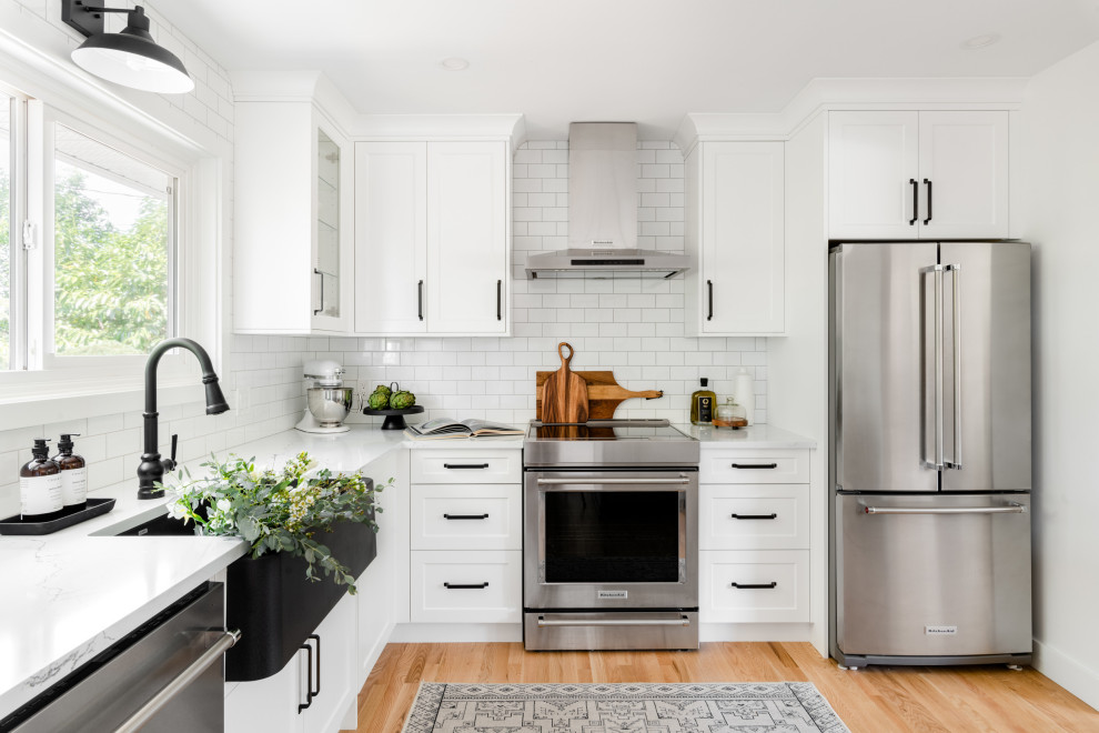 Inspiration for a small transitional l-shaped light wood floor and yellow floor eat-in kitchen remodel in Vancouver with a farmhouse sink, shaker cabinets, white cabinets, quartz countertops, white backsplash, ceramic backsplash, stainless steel appliances, an island and white countertops