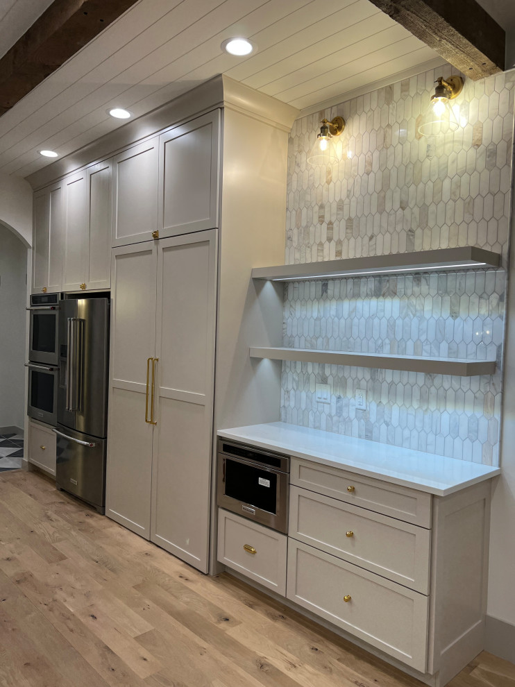 Large transitional l-shaped light wood floor and shiplap ceiling kitchen photo with a farmhouse sink, shaker cabinets, beige cabinets, quartz countertops, gray backsplash, marble backsplash, stainless steel appliances, an island and white countertops