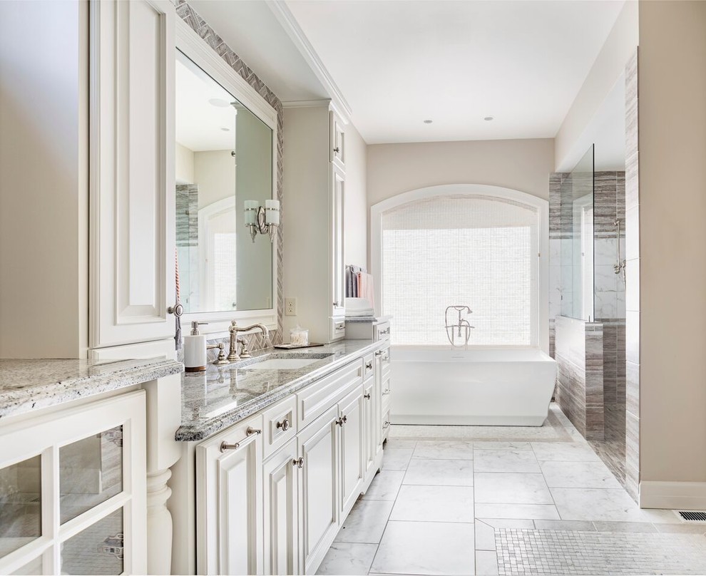 This is an example of a mid-sized traditional master bathroom in DC Metro with light wood cabinets, a freestanding tub, a curbless shower, a one-piece toilet, beige tile, mosaic tile, ceramic floors, an undermount sink, marble benchtops, beige walls, raised-panel cabinets, white floor, an open shower and grey benchtops.