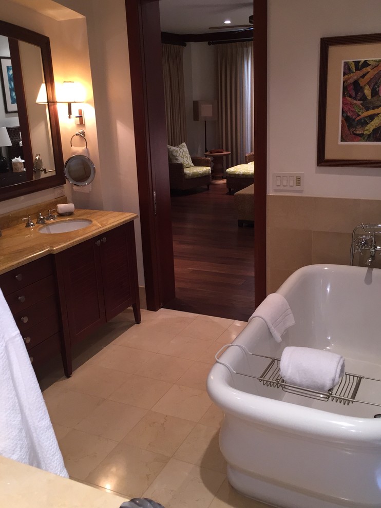 Photo of a large traditional master bathroom in Hawaii with an undermount sink, recessed-panel cabinets, dark wood cabinets, marble benchtops, a freestanding tub, a corner shower, a two-piece toilet, beige tile, stone tile, white walls and limestone floors.