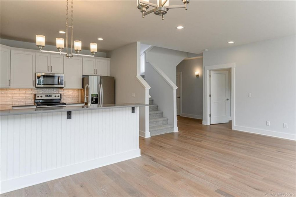 Open concept kitchen - mid-sized transitional u-shaped vinyl floor and brown floor open concept kitchen idea with an undermount sink, white cabinets, quartzite countertops, stainless steel appliances, a peninsula and gray countertops