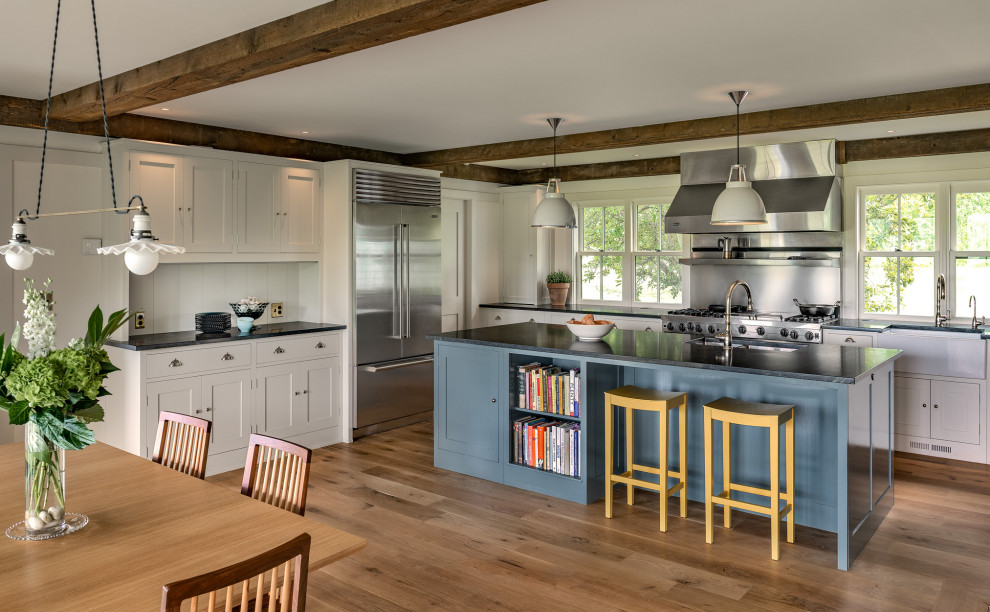 Country u-shaped eat-in kitchen in New York with shaker cabinets, white cabinets, stainless steel appliances, medium hardwood floors, with island, brown floor and black benchtop.