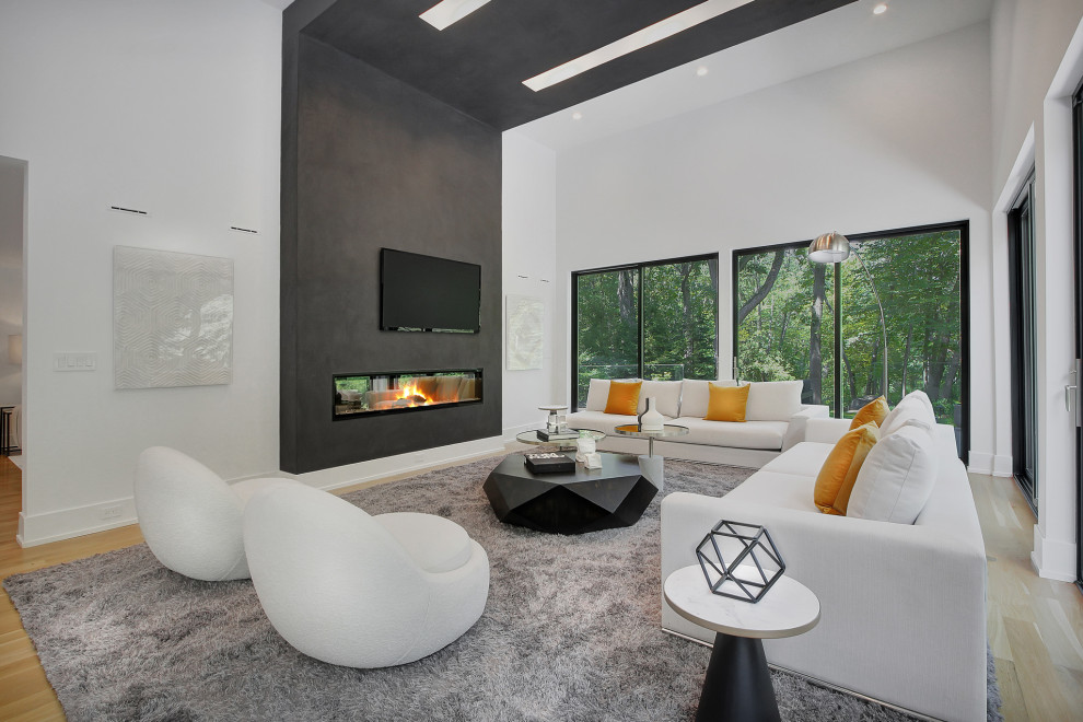 This is an example of a large contemporary open plan games room in New York with white walls, light hardwood flooring, a hanging fireplace, a concrete fireplace surround, a wall mounted tv and a vaulted ceiling.