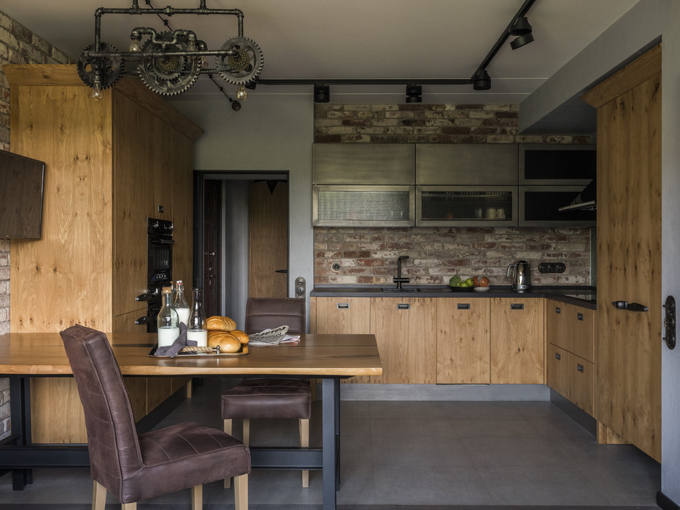 Photo of an industrial l-shaped eat-in kitchen in Moscow with an undermount sink, flat-panel cabinets, light wood cabinets, brown splashback, brick splashback, black appliances, grey floor, black benchtop and no island.