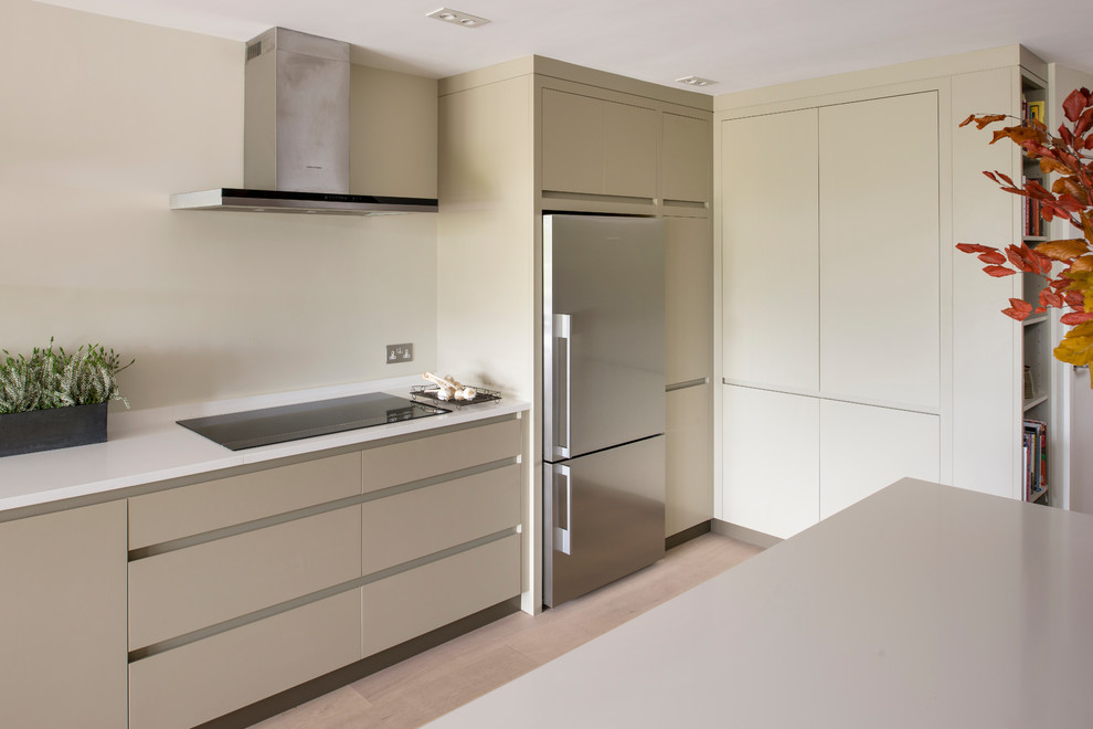 This is an example of a medium sized modern l-shaped kitchen/diner in Sussex with flat-panel cabinets, beige cabinets, quartz worktops, white splashback, stainless steel appliances, light hardwood flooring and an island.