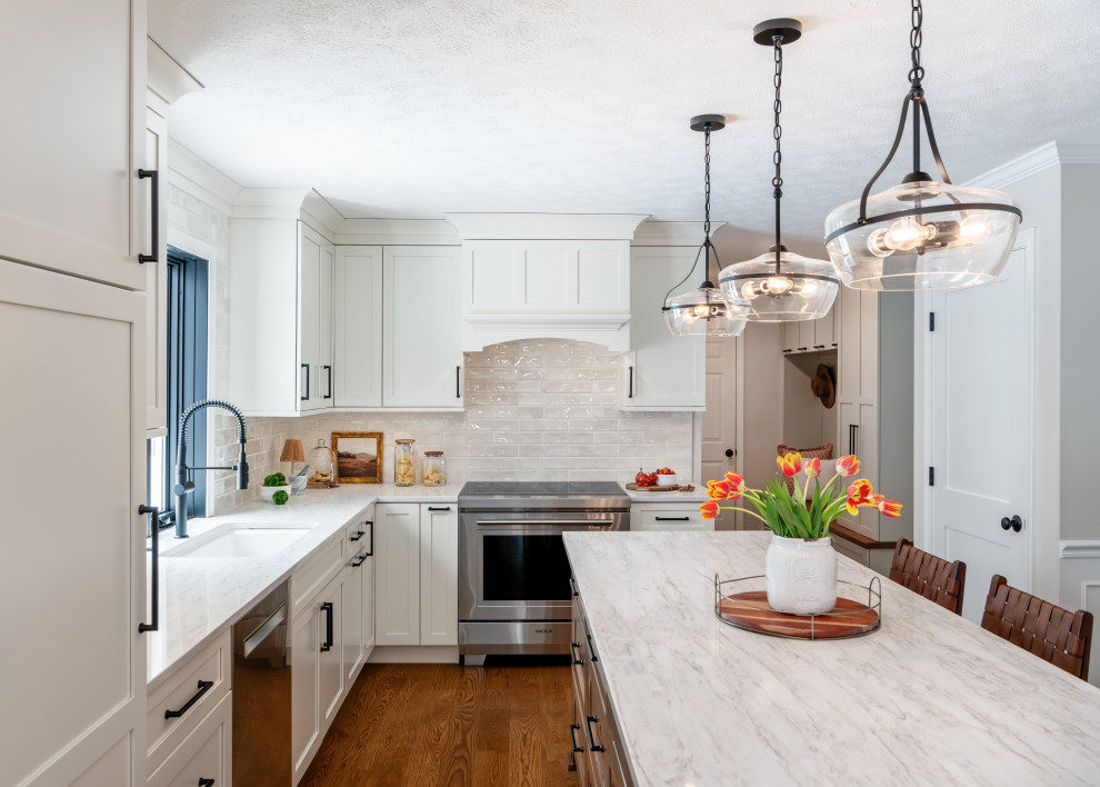 Kitchen - transitional l-shaped medium tone wood floor and brown floor kitchen idea in Boston with an undermount sink, shaker cabinets, white cabinets, white backsplash, subway tile backsplash, stainless steel appliances, an island and white countertops