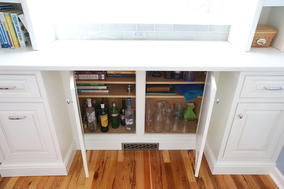 Example of a small transitional u-shaped medium tone wood floor, brown floor and vaulted ceiling kitchen pantry design in Omaha with a farmhouse sink, raised-panel cabinets, white cabinets, solid surface countertops, multicolored backsplash, mosaic tile backsplash, stainless steel appliances, no island and white countertops