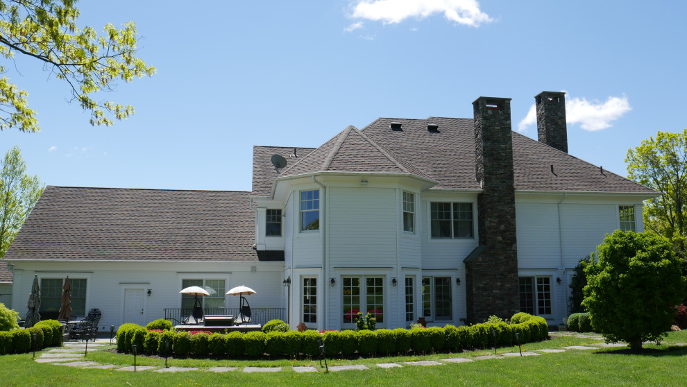 На фото: огромный, четырехэтажный, белый частный загородный дом в классическом стиле с коричневой крышей