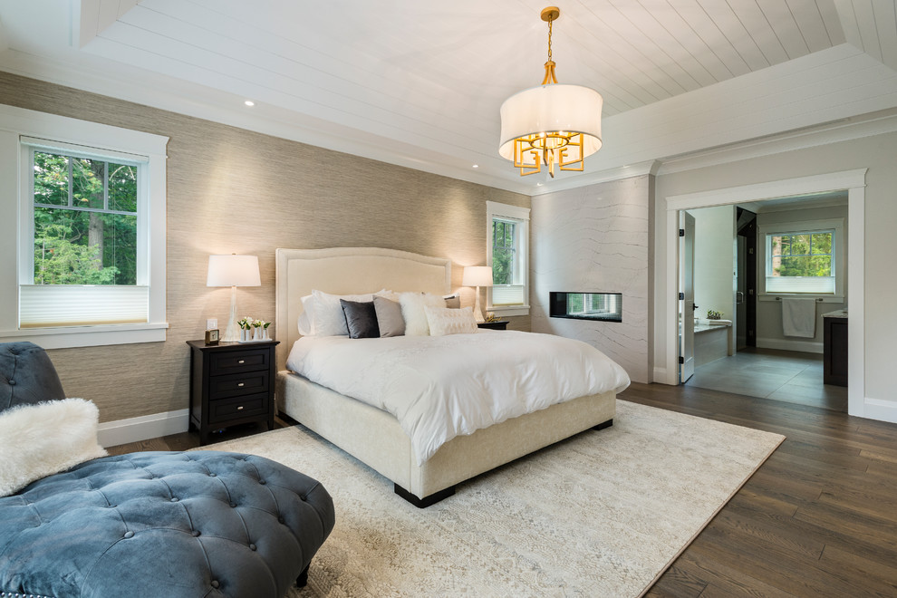 This is an example of a large traditional master bedroom in Vancouver with white walls, medium hardwood floors, a two-sided fireplace, a stone fireplace surround and brown floor.