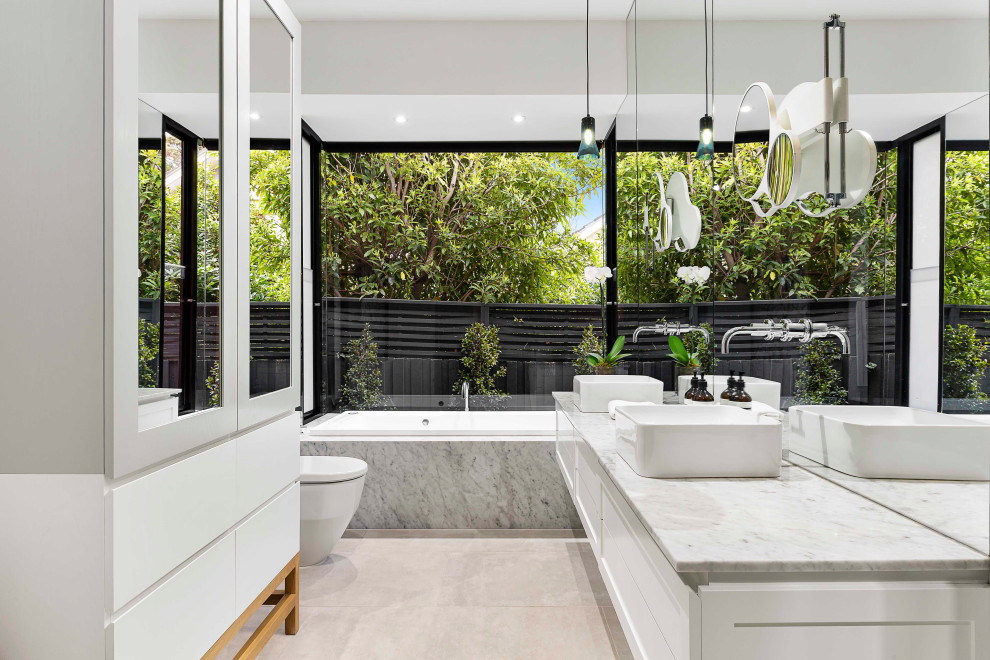 This is an example of a mid-sized contemporary master bathroom in Melbourne with shaker cabinets, white cabinets, white walls, porcelain floors, a vessel sink, marble benchtops, grey floor, white benchtops and a drop-in tub.
