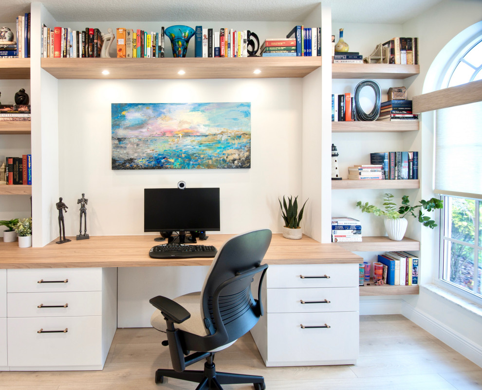 This is an example of a large beach style study room in Miami with white walls, laminate floors, a built-in desk and beige floor.