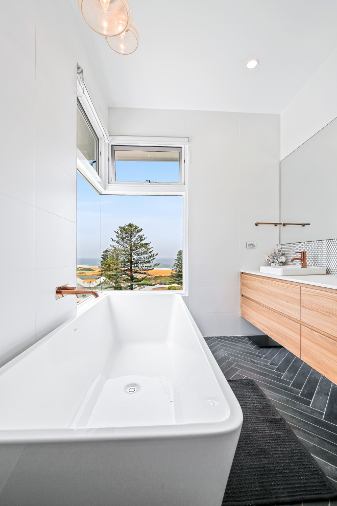 Design ideas for a large beach style master bathroom in Central Coast with flat-panel cabinets, light wood cabinets, a freestanding tub, white walls, a vessel sink, black floor, white benchtops, a single vanity and a floating vanity.