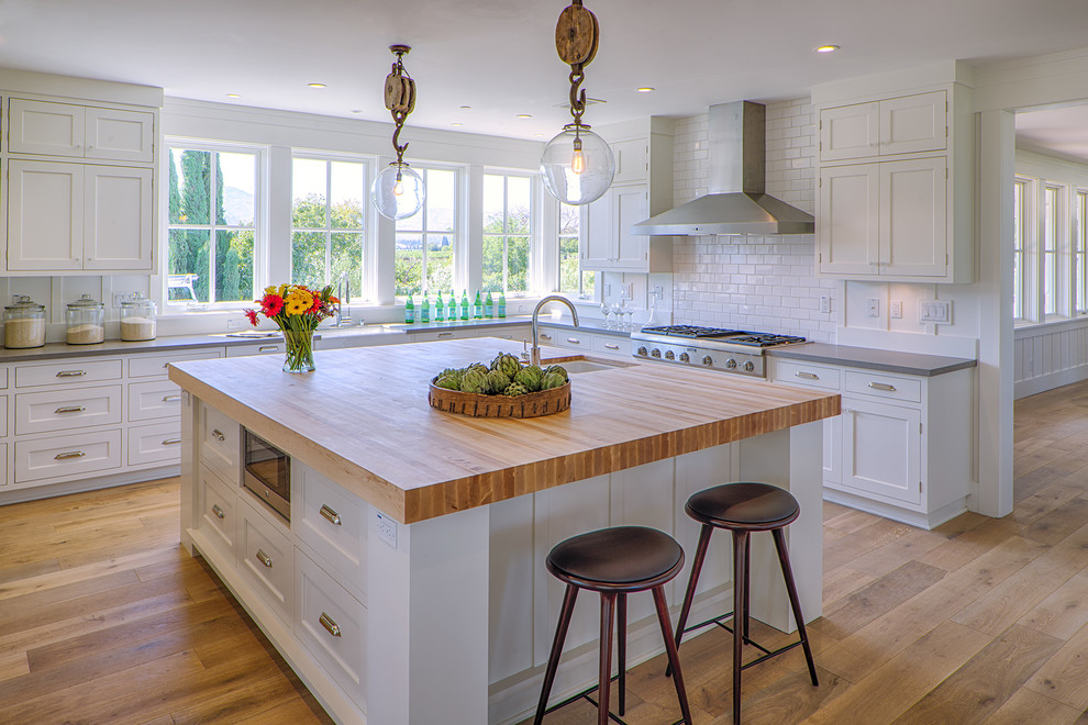 Photo of a country u-shaped kitchen in San Francisco with an undermount sink, shaker cabinets, white cabinets, white splashback, subway tile splashback, stainless steel appliances, medium hardwood floors and with island.