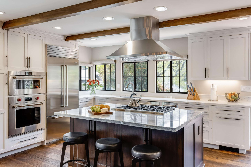Photo of a mediterranean kitchen/diner in San Francisco with shaker cabinets, white cabinets, stainless steel appliances, medium hardwood flooring, an island, brown floors, white worktops, exposed beams and granite worktops.