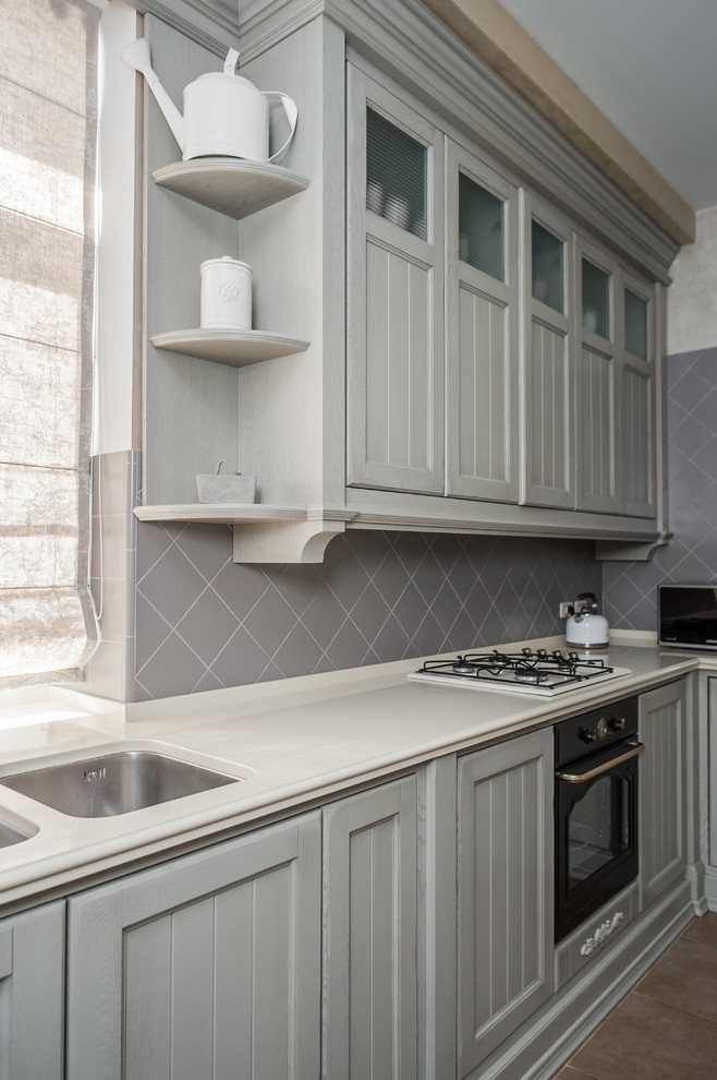This is an example of a mid-sized traditional single-wall eat-in kitchen in Other with an undermount sink, grey cabinets, solid surface benchtops, grey splashback, cement tile splashback, black appliances, ceramic floors, with island, brown floor, beige benchtop and shaker cabinets.