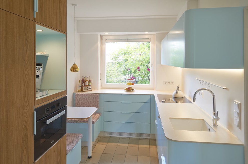Small contemporary u-shaped separate kitchen in Cologne with an integrated sink, flat-panel cabinets, blue cabinets, white splashback, black appliances, no island, beige floor and white benchtop.