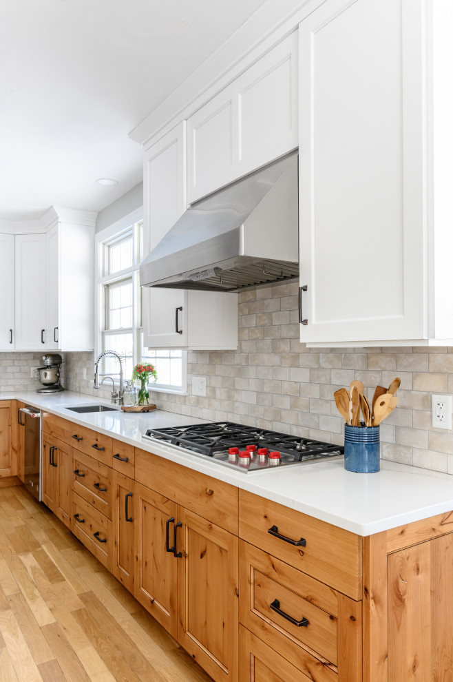 This is an example of a large country l-shaped eat-in kitchen in Boston with an undermount sink, recessed-panel cabinets, white cabinets, quartz benchtops, beige splashback, ceramic splashback, stainless steel appliances, light hardwood floors, with island, brown floor and white benchtop.