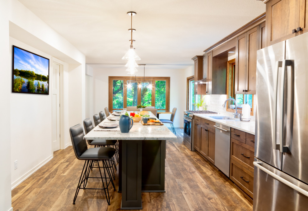 Mid-sized traditional galley eat-in kitchen in Minneapolis with a double-bowl sink, shaker cabinets, medium wood cabinets, granite benchtops, white splashback, ceramic splashback, stainless steel appliances, vinyl floors, with island and white benchtop.