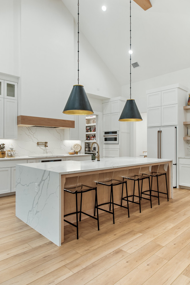 Inspiration for a mid-sized scandinavian l-shaped open plan kitchen in Dallas with a farmhouse sink, shaker cabinets, white cabinets, quartz benchtops, white splashback, engineered quartz splashback, white appliances, vinyl floors, with island, white benchtop and exposed beam.