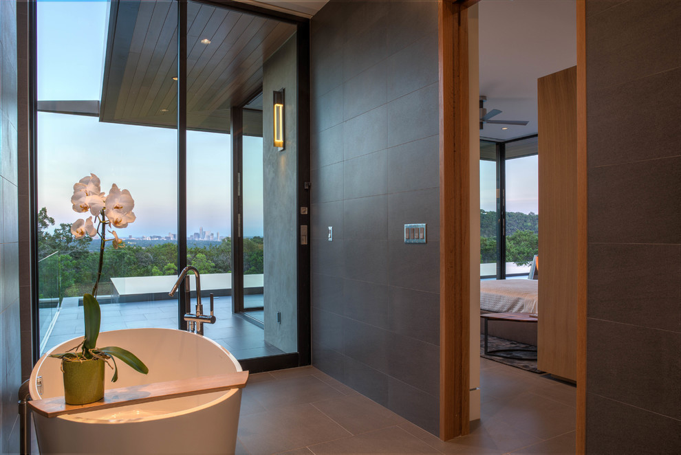 Photo of a large contemporary master bathroom in Austin with a freestanding tub, porcelain tile, porcelain floors, flat-panel cabinets, medium wood cabinets, an alcove shower, gray tile, grey walls, an undermount sink and marble benchtops.