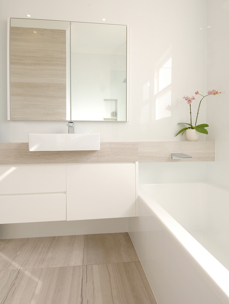 Пример оригинального дизайна: главная ванная комната среднего размера в стиле модернизм с плоскими фасадами, белыми фасадами, накладной ванной, душем в нише, унитазом-моноблоком, белой плиткой, керамической плиткой, белыми стенами, полом из известняка, настольной раковиной, столешницей из известняка, бежевым полом, открытым душем, бежевой столешницей, нишей, тумбой под одну раковину, подвесной тумбой, многоуровневым потолком и панелями на стенах