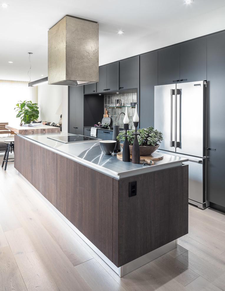 Photo of a mid-sized modern galley eat-in kitchen in Ottawa with an undermount sink, flat-panel cabinets, grey cabinets, stainless steel benchtops, grey splashback, stainless steel appliances, light hardwood floors and with island.