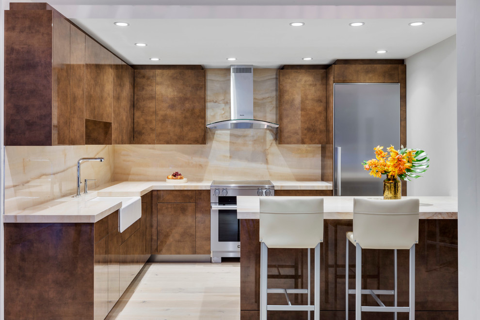 Mid-sized contemporary l-shaped eat-in kitchen in Boston with a farmhouse sink, brown cabinets, onyx benchtops, multi-coloured splashback, stone slab splashback, stainless steel appliances, light hardwood floors, a peninsula and flat-panel cabinets.