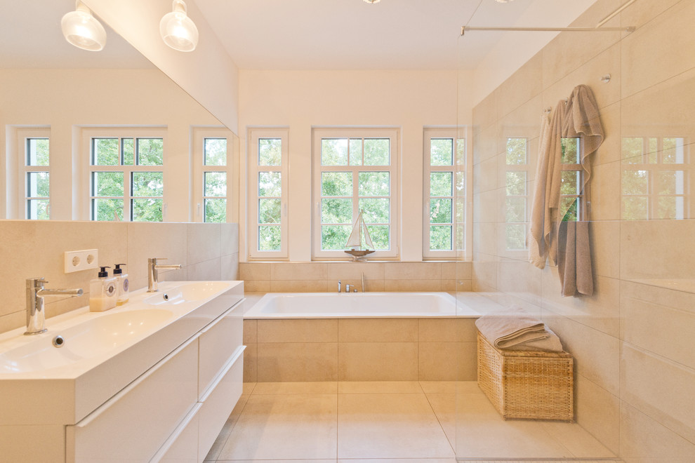 Photo of a large contemporary bathroom in Hanover with a drop-in tub, a curbless shower, a wall-mount toilet, beige tile, ceramic tile, white walls, pebble tile floors and a trough sink.
