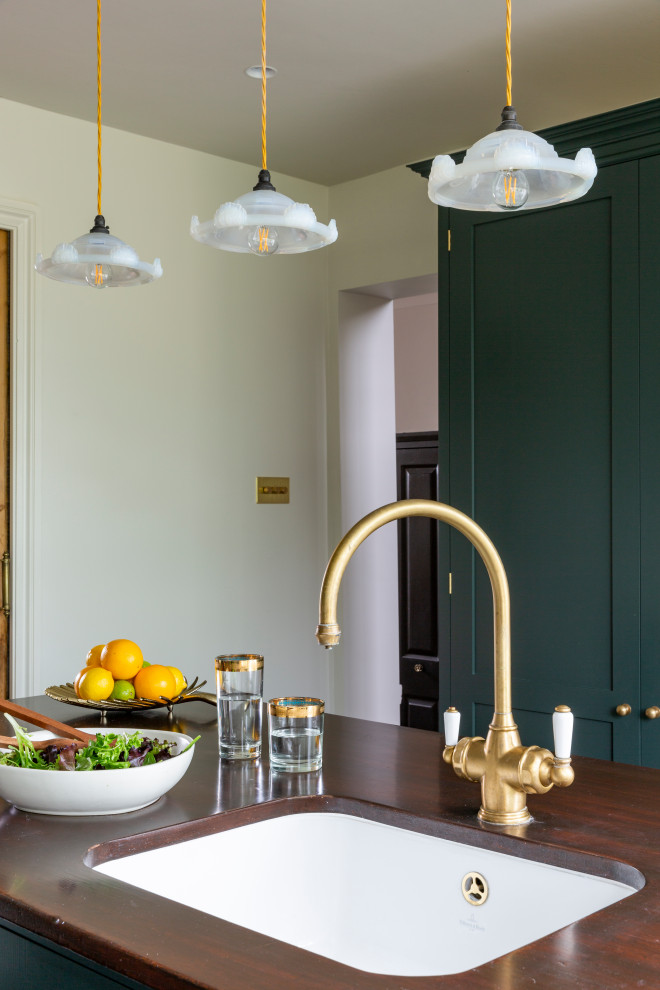 Mid-sized eclectic single-wall eat-in kitchen in London with a farmhouse sink, shaker cabinets, green cabinets, quartzite benchtops, metallic splashback, marble splashback, black appliances, dark hardwood floors, with island, brown floor and white benchtop.