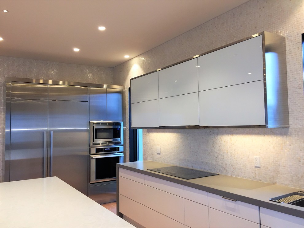 Contemporary eat-in kitchen in New York with flat-panel cabinets, white cabinets, quartz benchtops, stainless steel appliances, medium hardwood floors, with island and grey benchtop.