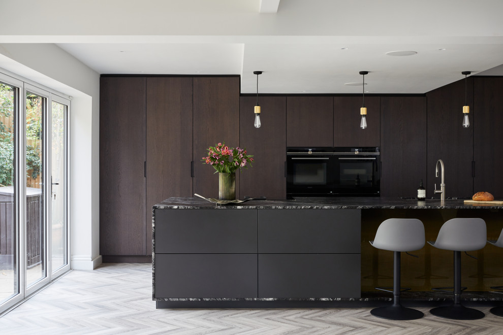 Large contemporary single-wall open plan kitchen in London with a submerged sink, flat-panel cabinets, granite worktops, stainless steel appliances, light hardwood flooring, an island, grey floors and black worktops.