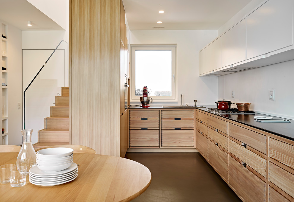 Design ideas for a mid-sized contemporary u-shaped eat-in kitchen in Other with a drop-in sink, flat-panel cabinets, light wood cabinets, brown floor, white splashback, concrete floors and no island.
