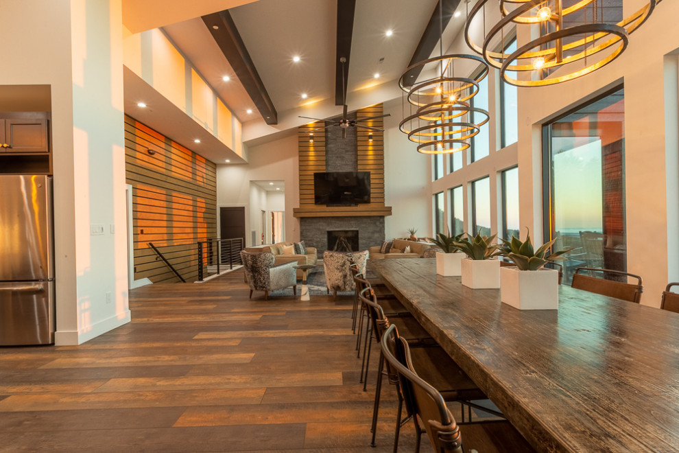 Idée de décoration pour une très grande salle à manger ouverte sur le salon minimaliste en bois avec un mur blanc, une cheminée standard, un manteau de cheminée en pierre, un sol marron, un plafond voûté et un sol en vinyl.