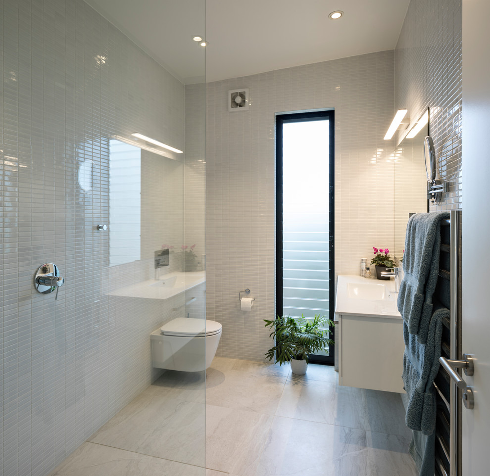 This is an example of a mid-sized contemporary 3/4 wet room bathroom in Other with flat-panel cabinets, white cabinets, a wall-mount toilet, gray tile, ceramic tile, grey walls, ceramic floors, a console sink, solid surface benchtops, grey floor, an open shower and white benchtops.
