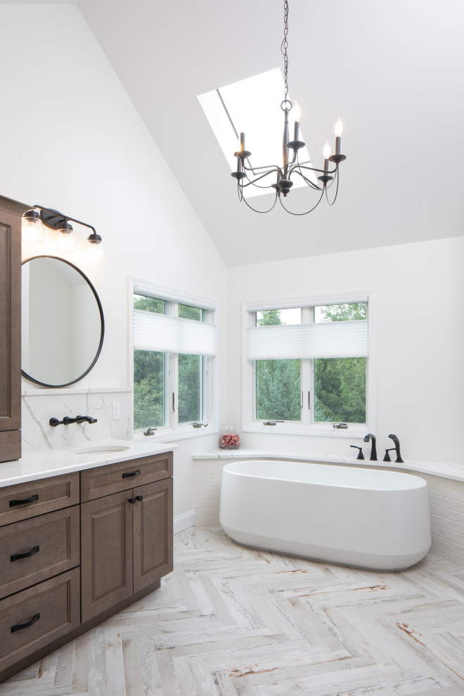 Inspiration for a large transitional master bathroom in New York with raised-panel cabinets, medium wood cabinets, white tile, white walls, ceramic floors, an undermount sink, engineered quartz benchtops, white benchtops, a double vanity, a built-in vanity, a freestanding tub, grey floor and vaulted.