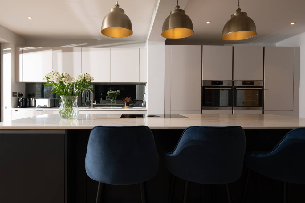 Design ideas for a mid-sized modern single-wall kitchen in Hertfordshire with an integrated sink, flat-panel cabinets, white cabinets, quartzite benchtops, black appliances, light hardwood floors, with island, brown floor and white benchtop.