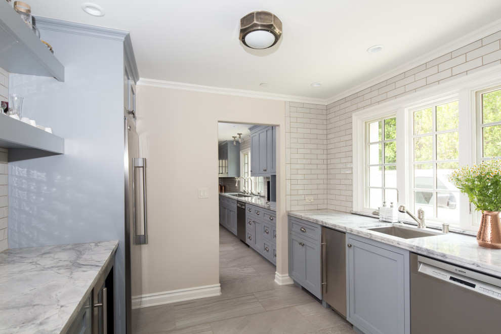 Large transitional u-shaped porcelain tile and gray floor enclosed kitchen photo in Los Angeles with a drop-in sink, shaker cabinets, quartzite countertops, white backsplash, ceramic backsplash, stainless steel appliances, an island and gray countertops