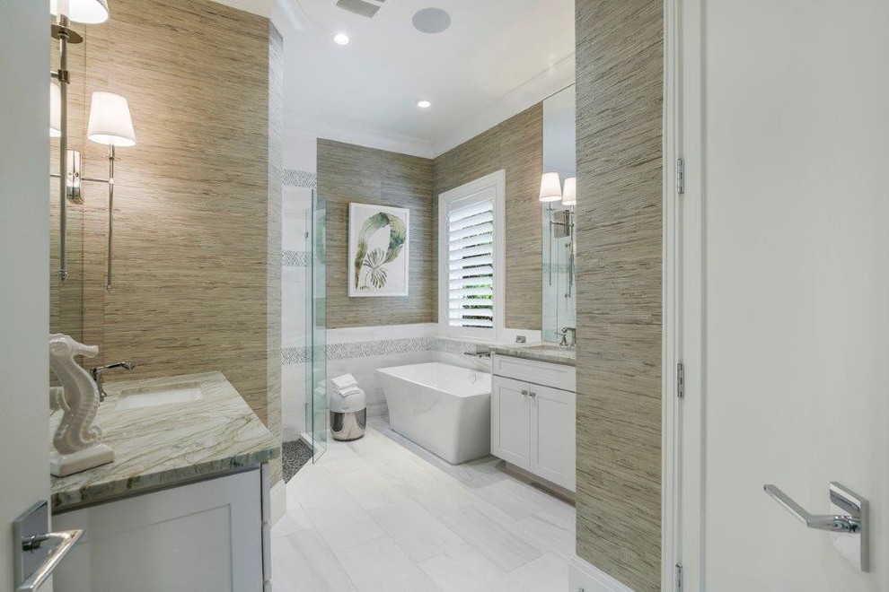 Inspiration for a mid-sized beach style master bathroom in Miami with shaker cabinets, white cabinets, an open shower, a one-piece toilet, white tile, beige walls, porcelain floors, an integrated sink, engineered quartz benchtops and a freestanding tub.