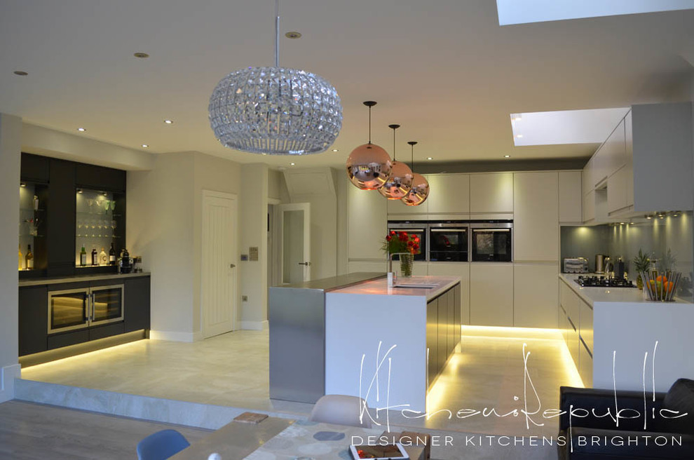 Inspiration for a large modern eat-in kitchen in Sussex with an undermount sink, flat-panel cabinets, grey cabinets, solid surface benchtops, blue splashback, glass sheet splashback, stainless steel appliances, travertine floors and with island.