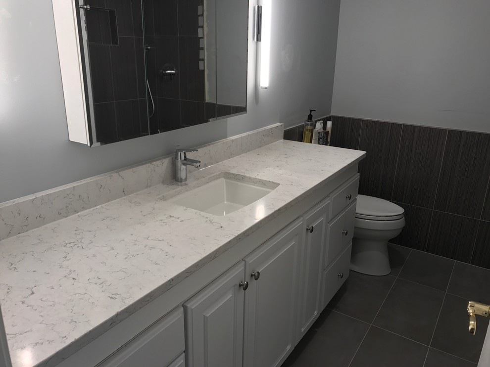 Mid-sized transitional 3/4 black tile and porcelain tile laminate floor and black floor alcove shower photo with raised-panel cabinets, white cabinets, a two-piece toilet, gray walls, an undermount sink, marble countertops and white countertops