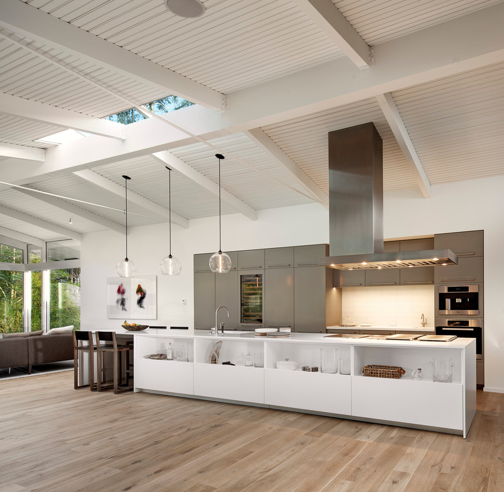 This is an example of a large midcentury galley open plan kitchen in Santa Barbara with flat-panel cabinets, grey cabinets, white splashback, medium hardwood floors, with island, stainless steel appliances and beige floor.