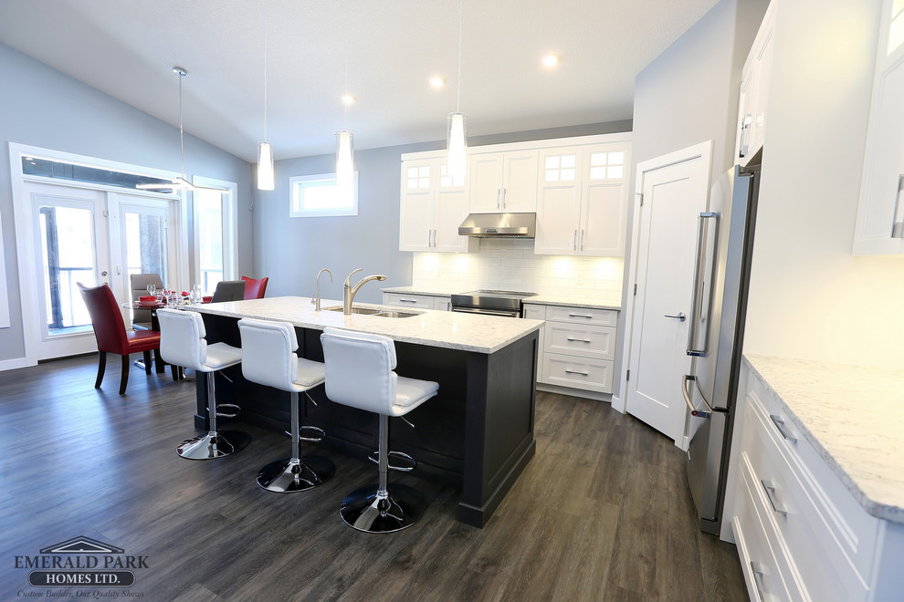 Example of a l-shaped vinyl floor and gray floor eat-in kitchen design in Other with an undermount sink, shaker cabinets, white cabinets, quartz countertops, white backsplash, ceramic backsplash, stainless steel appliances and an island