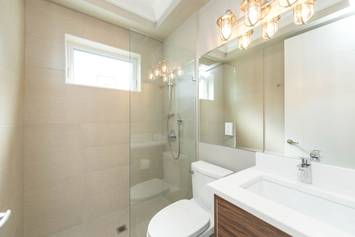 Photo of a mid-sized transitional 3/4 bathroom in Vancouver with flat-panel cabinets, dark wood cabinets, an alcove tub, a shower/bathtub combo, a two-piece toilet, beige tile, porcelain tile, beige walls, an undermount sink, solid surface benchtops and a sliding shower screen.
