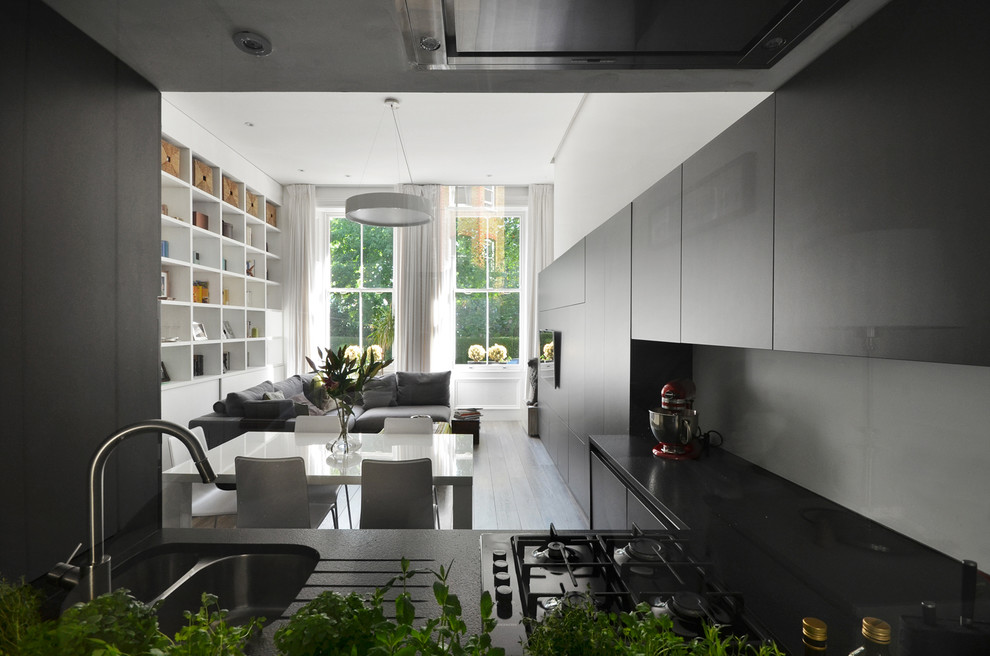 Small contemporary l-shaped open plan kitchen in London with a double-bowl sink, flat-panel cabinets, no island, grey floor and black benchtop.
